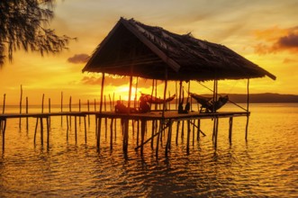 Native people relaxing in hammocks on wooden jetty during sunset on Kri island, Raja Ampat, West