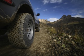 Close-up A large off-road all-terrain car wheel stands on a rough road in the mountains against the