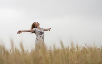 Happy woman in a floral dress stands amidst golden wheat, enjoying the serene landscape