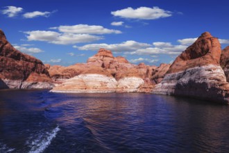 The foamy trace from powerboat crosses emerald waters. Hills from red sandstone surround the lake.