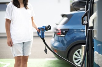 Woman charge her Electric car on gas station. Blue car and electric plug for charging. Ecology