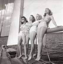 1940s sailing boat. Four young women are standing and leaning against the sails of the boat and