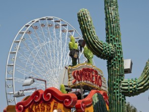 Colourful amusement park with a large Ferris wheel and decorative cacti under a clear sky, Vienna,