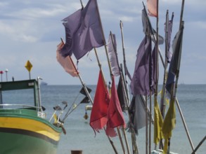 Colourful flags waving in the wind, next to a green boat in front of a wide sea and blue sky,