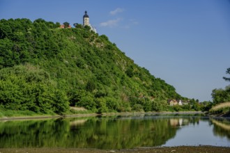 River with green hill and church in the background, small village houses reflected in the water,