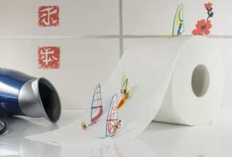 Indoor surfing by little world miniatures on toilet paper with hairdryer as background for the wind