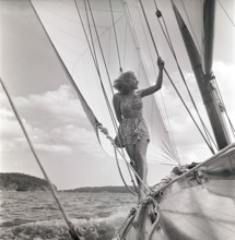 1940s sailing boat. A young woman is aboard a fashionable sailing boat and is standing on deck when
