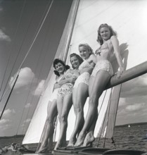 1940s sailing boat. Four young women are standing and leaning against the sails of the boat and