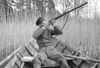 In the 1930s. A man sits in a rowing boat and aims his rifle upwards to shoot ducks. Sweden 1939.