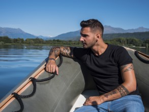 Portrait of young handsome man with tattooed body looking at camera sailing in boat