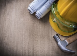 Claw hammer goggles blueprints and safety cap on wooden background
