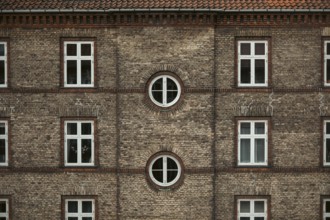 Symmetrical brick building façade with square and round windows, displaying traditional