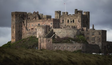 Bamburgh Castle, a medieval stone castle stands majestically under a cloudy sky, surrounded by