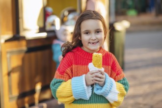 Caucasian little cute girl eating delicious tasty corn on the cob in city park