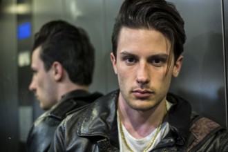 Handsome young man leaning against mirror inside an elevator or lift, looking at camera