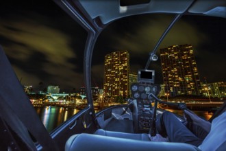 Helicopter cockpit flies in Honolulu skyline by night, Oahu, Hawaii, with pilot arm and control