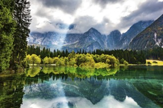 The sun's rays break through the clouds. The smooth surface of the water reflects forest and