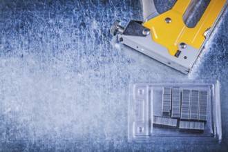 Yellow stapler gun chrome staples on scratched metallic background