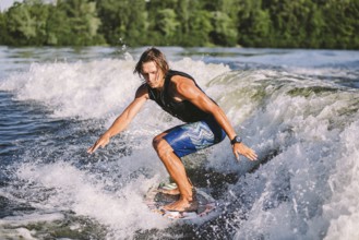 Young athletic man with long hair wakesurfing on waves of river in sunny summer weather. Ttheme