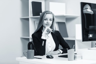 Young pretty business woman sitting at the desk with computer in blue office
