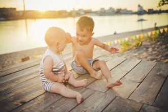 Two little boys sitting on the pier on the river bank. Concept of friendship and fraternity. Sunny