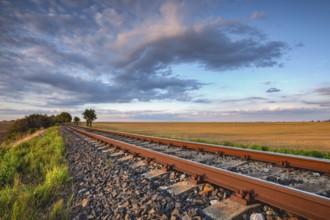Old Railway tracks running through a field stretch to rural countryside at sunset. Single railway