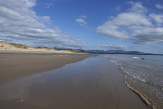 Beach and dunes with calm sea, in the background the mountains of Snowdonia National Park, Ynys