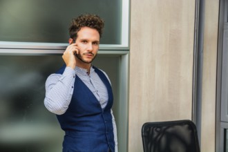 Handsome businessman in his office talking on cell phone, looking at camera, serious