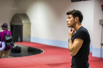 Young man standing in the airport waiting for his baggage at luggage claim belt