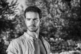 Ruggedly Handsome Man Among Trees with Shirt Unbuttoned Relaxing in Warm Sunlight