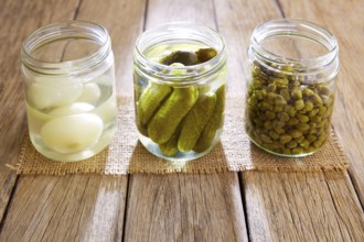 Bottled pickles as capers onion and cucumbers in wooden table