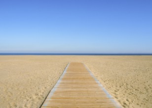 A yellow-blue picture, where the blue half is sky and the yellow half is sand and a wooden path on