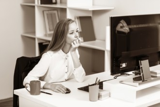 Young pretty business woman sitting at the desk with computer in blue office
