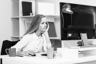 Young pretty business woman sitting at the desk with computer in blue office
