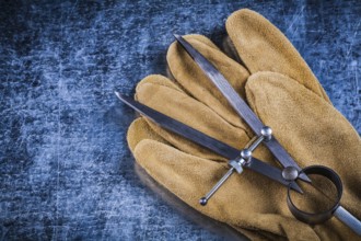 Pair of construction compasses leather protective gloves on metallic background