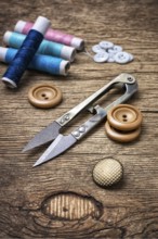 Scissors, thread and buttons on unhewn darianna background in vintage style