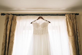 The bride's dress hangs on the cornice on the window