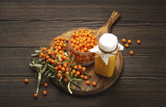 Sea buckthorn healthy drink in bottle, ripe berries in glass jar and branches with leaves top view