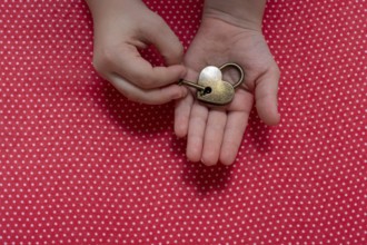 Hand holding a heart shaped lock and key on a red background