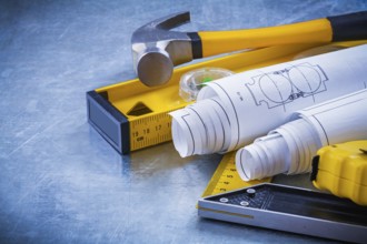 Close up image of hammer measuring line construction plans and level square ruler on metallic