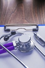 Stethoscope with purple tubes and ballpoint pen on paper in clipboard and vintage wooden board