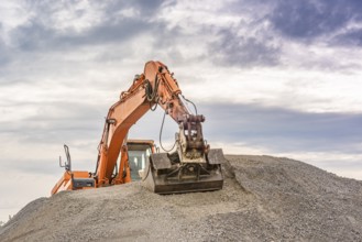 Frontal view of an orange excavator climbed on top of a ballast pile