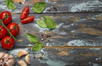 Food cooking border with cherry tomatoes, fresh green basil and garlic cloves top view on rustic