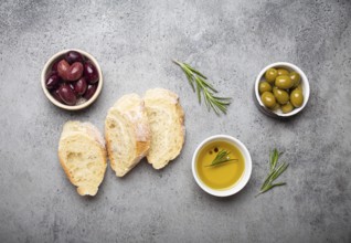 Slices of fresh ciabatta, green and brown olives, olive oil with rosemary, olive tree branches on