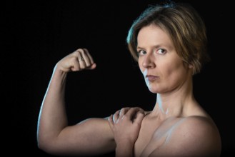 Low key studio portrait of a 35 year old white woman with naked shoulders showing her biceps,