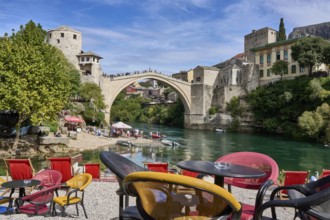 Cafe with colourful chairs on the bank of the river Neretva, behind the bridge Stari Most, numerous
