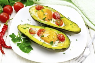 Scrambled eggs with cherry tomatoes in two halves of avocado in a plate, kitchen towel and fork on