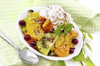 Fruit salad with orange, kiwi, cranberries and baked pumpkin, whipped cream, sprinkled with