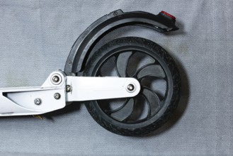 Close-up of a scooter's rear wheel with a sleek black tire and metal frame on a grey background