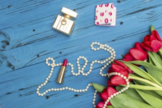 Red tulips in the necklace, lipstick and bottle of perfume on the background of blue wooden board